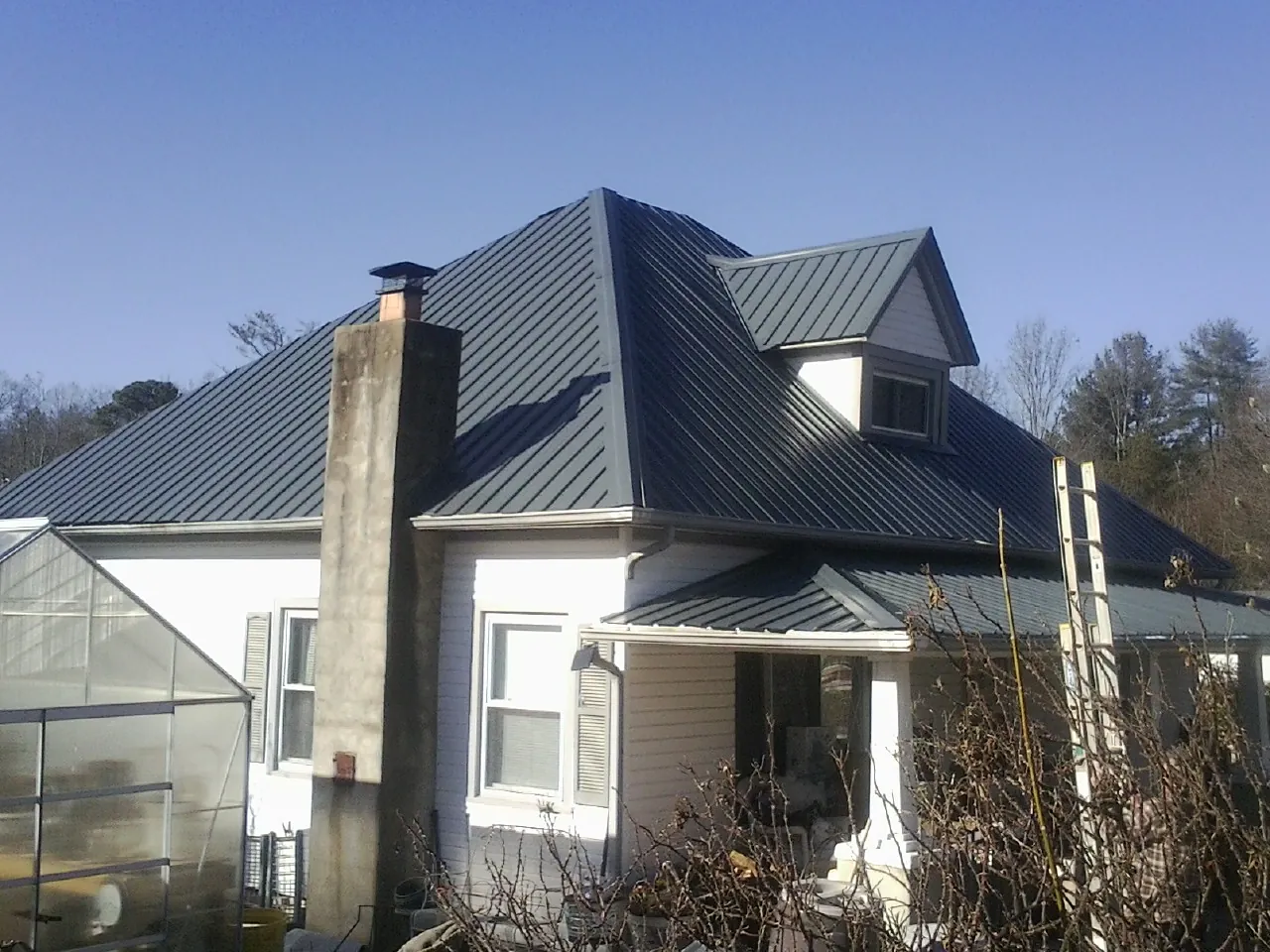 Dark blue standing seam metal roof on a white farmhouse with dormer — Slate & Tile Roof Repair by Roofing Brothers in Ponca City