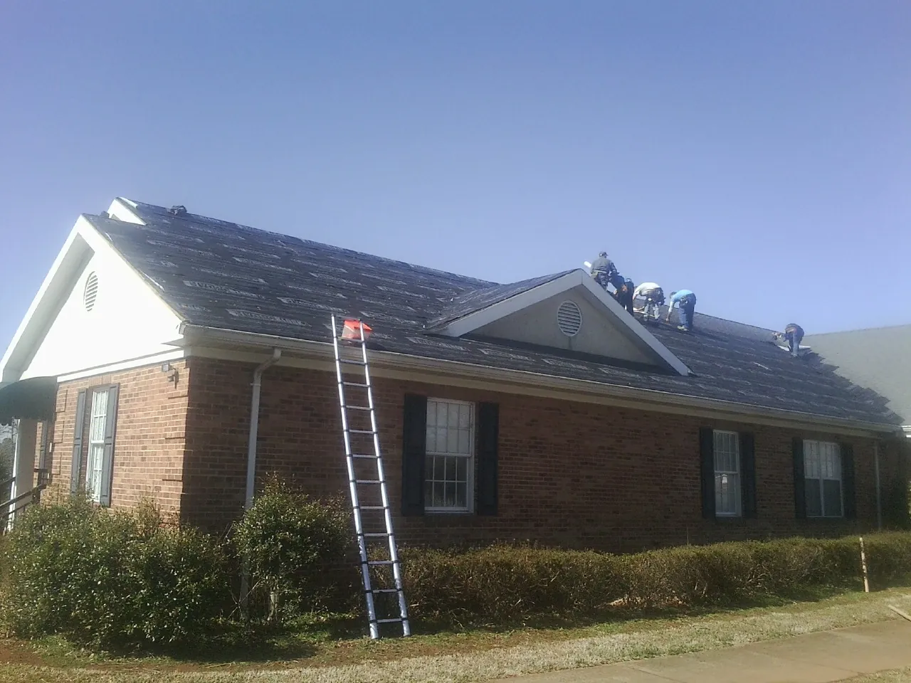 Crew tearing shingles off a brick ranch roof with a ladder set — Metal Roof Repair work by our crew in Ponca City