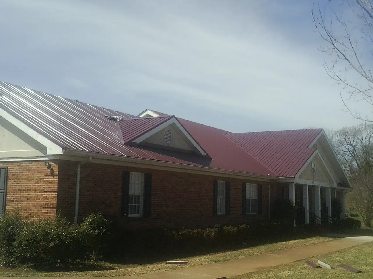 Red metal roof with gabled entries on a long brick building, from a Hail Damage Roof Repair job in Ponca City
