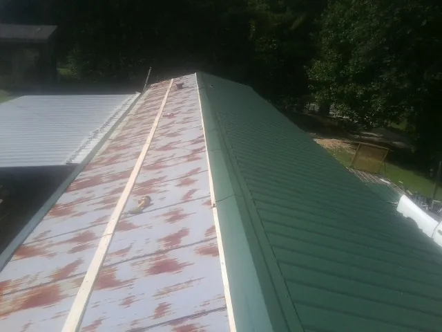 Old rusted panels beside newly installed green metal roofing — Wind Damage Roof Repair by Roofing Brothers in Ponca City