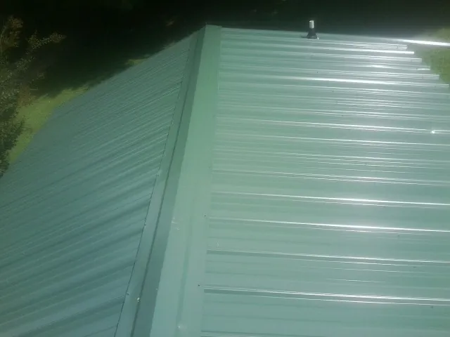 New green metal panels meeting at the ridge of a roof — Flat Roof Repair work by our crew in Ponca City
