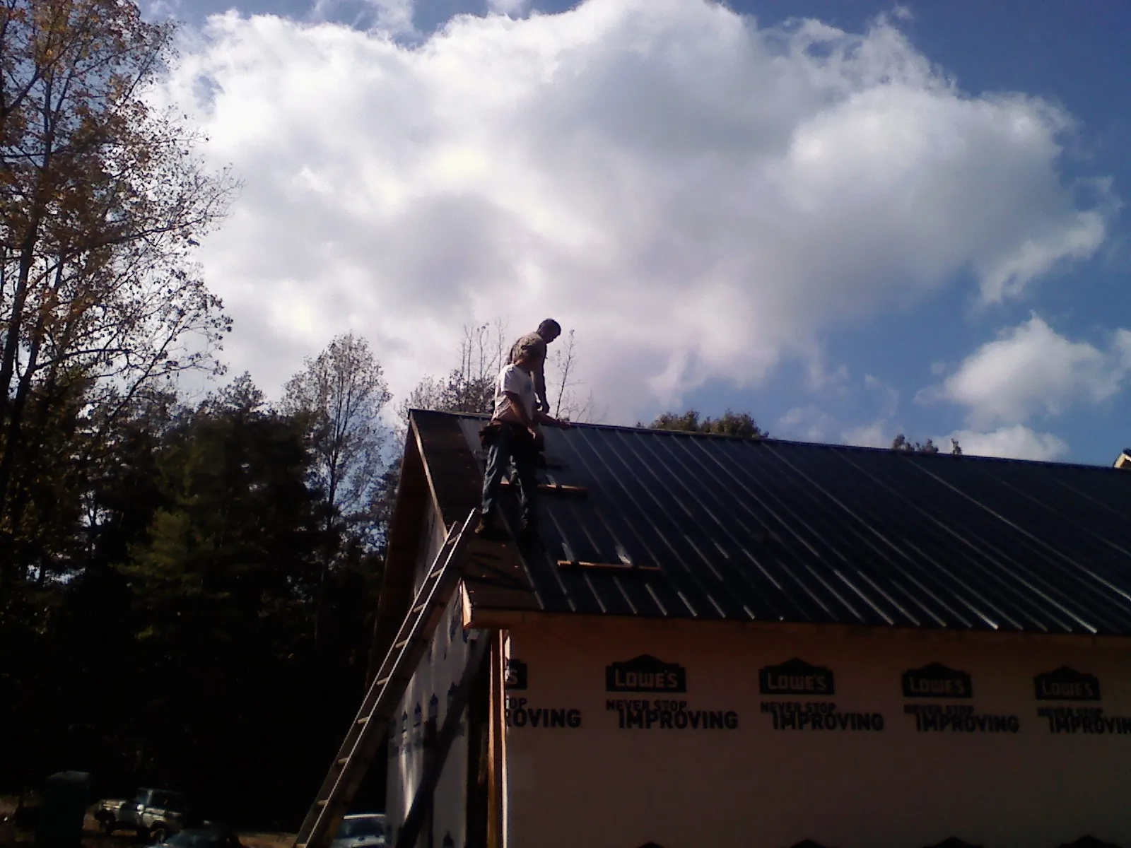 Roofer fastening dark metal panels high against a cloudy sky, from a Roof Inspection job in Ponca City