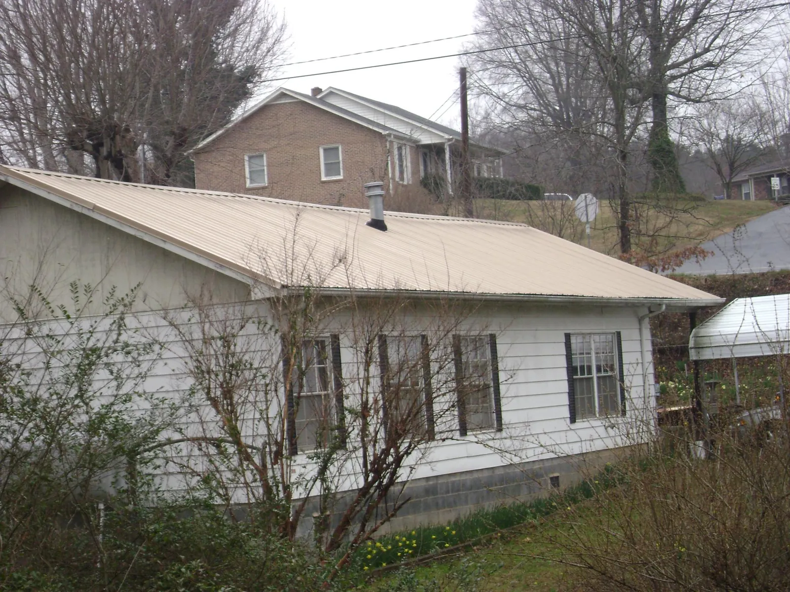 Tan metal roof on a white sided house set into a hillside — Commercial Roofing by Roofing Brothers in Ponca City