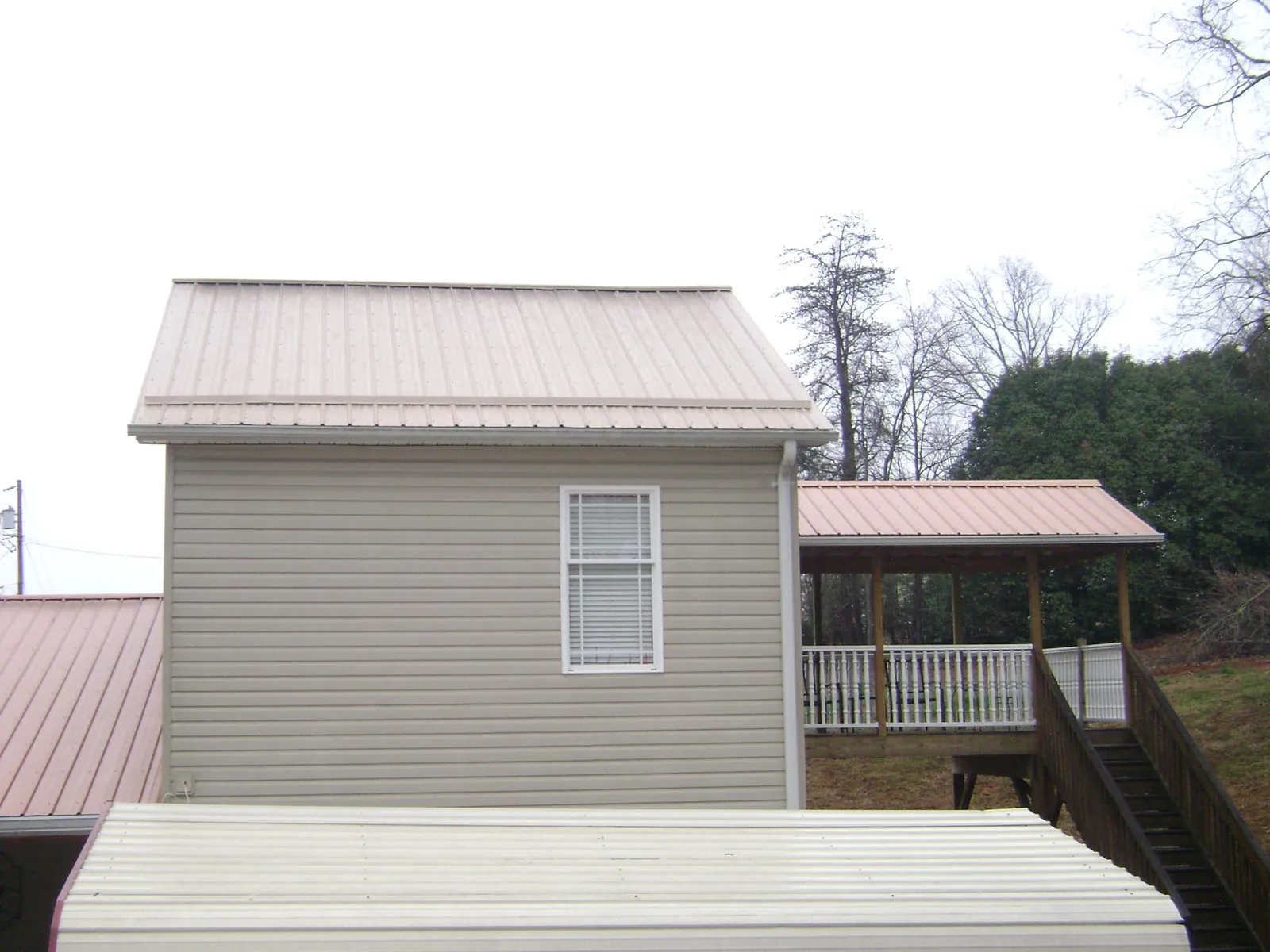 Tan metal roofs on a two story addition and attached porch, from a Roof Replacement job in Ponca City